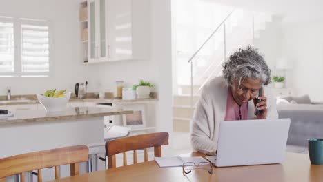 Retrato-De-Una-Anciana-Afroamericana-Sentada-En-La-Mesa,-Usando-Una-Computadora-Portátil-Y-Hablando-Por-Teléfono-Inteligente