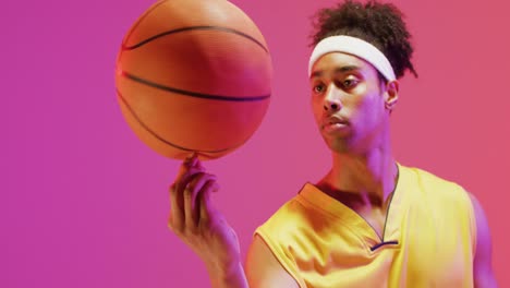 Video-of-biracial-male-basketball-player-spinning-ball-on-orange-to-pink-background
