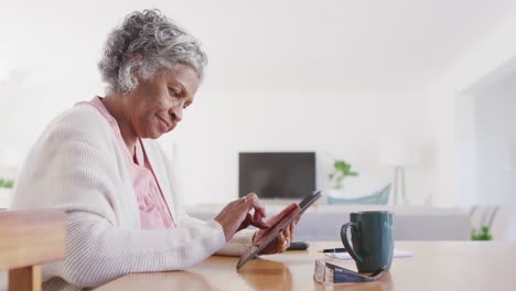 Portrait-of-senior-african-american-woman-sitting-at-table,-using-tablet