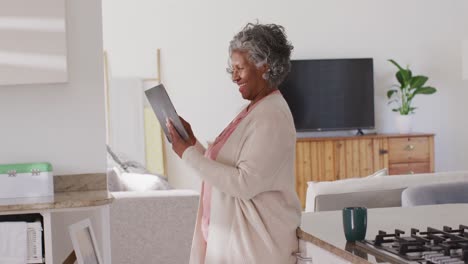 Portrait-of-happy-senior-african-american-woman-using-tablet-in-kitchen