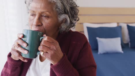 Glückliche-ältere-Afroamerikanische-Frau,-Die-Durch-Das-Fenster-Schaut-Und-Kaffee-Trinkt