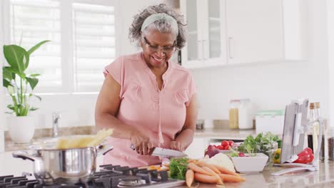 Glückliche-ältere-Afroamerikanische-Frau,-Die-In-Der-Küche-Kocht-Und-Gemüse-Hackt