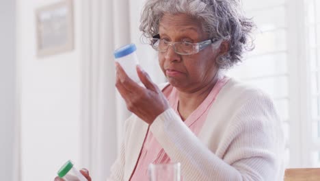 Senior-african-american-woman-sitting-at-table,-taking-pills