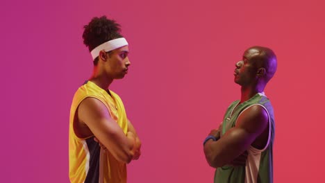 Video-of-two-diverse-male-basketball-players-facing-each-other-on-pink-background