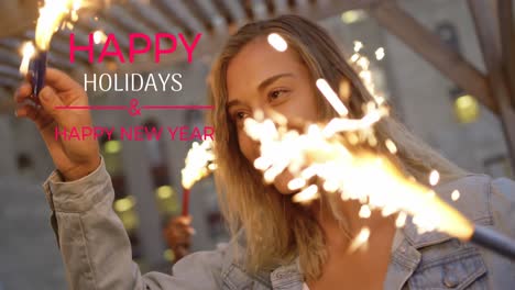 Animation-of-happy-holidays-and-new-year-text-over-smiling-caucasian-woman-holding-sparklers