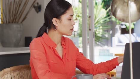 Biracial-woman-sitting-at-table-and-working-with-laptop