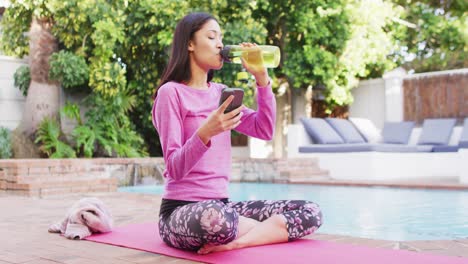 Mujer-Birracial-Practicando-Yoga-Y-Bebiendo-Agua-En-El-Jardín.