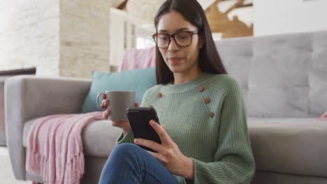 Biracial-woman-using-smartphone-and-smiling-in-living-room