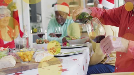 Animation-of-yellow-light-spots-over-caucasian-senior-man-pouring-wine-at-christmas-dinner-table