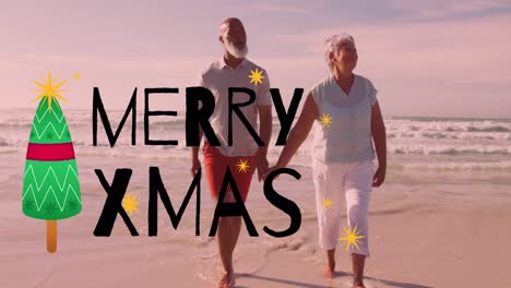 Animation-of-merry-xmas-text-over-happy-diverse-senior-couple-holding-hands-walking-on-sunny-beach