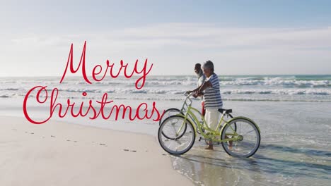 Animation-of-merry-christmas-text-over-diverse-senior-couple-with-bikes-on-sunny-beach