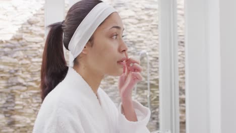 Biracial-woman-applying-cream-on-face-in-bathroom