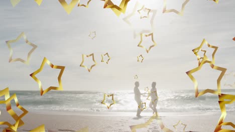 Animation-of-gold-christmas-stars-over-happy-silhouetted-couple-dancing-on-sunny-beach