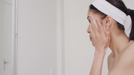 Biracial-woman-applying-cream-on-face-in-bathroom
