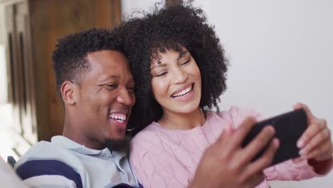 Glückliches-Afroamerikanisches-Paar,-Das-Gemeinsam-Sein-Smartphone-Im-Wohnzimmer-Nutzt