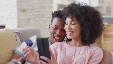 Glückliches-Afroamerikanisches-Paar,-Das-Gemeinsam-Sein-Smartphone-Im-Wohnzimmer-Nutzt