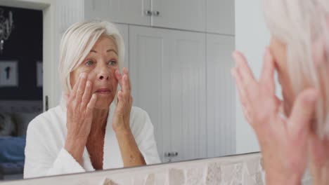 Glückliche-ältere-Kaukasische-Frau,-Die-Im-Badezimmer-In-Den-Spiegel-Schaut-Und-Ihr-Gesicht-Berührt