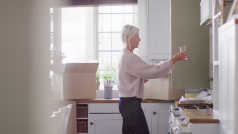 Happy-senior-caucasian-woman-moving-house,-unpacking-boxes-in-kitchen