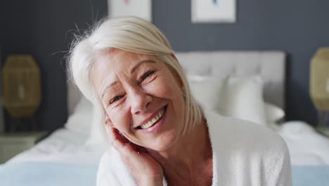 Portrait-of-happy-senior-caucasian-woman-sitting-on-bed-in-bedroom,-looking-at-camera