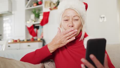 Glückliche-ältere-Kaukasische-Frau-Mit-Weihnachtsmannmütze,-Die-Ihr-Smartphone-Für-Videoanrufe-Nutzt
