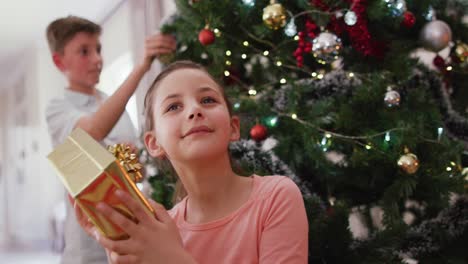 Happy-caucasian-siblings-decorating-christmas-tree-at-christmas