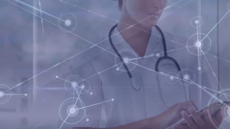 Animation-of-network-of-connections-with-icons-over-caucasian-female-doctor-with-tablet
