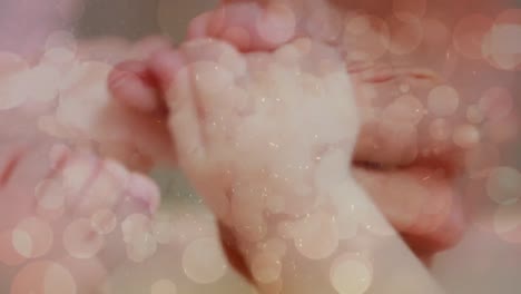 Animation-of-light-spots-over-baby-holding-hands