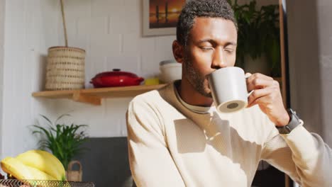 Happy-african-american-man-standing-in-kitchen,-drinking-coffee