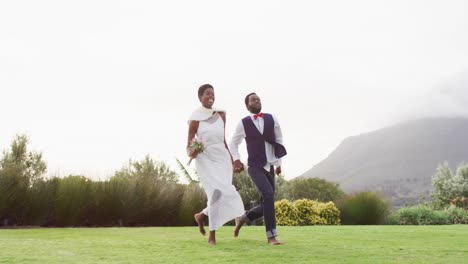 Happy-african-american-couple-holding-hands-and-jumping-during-wedding