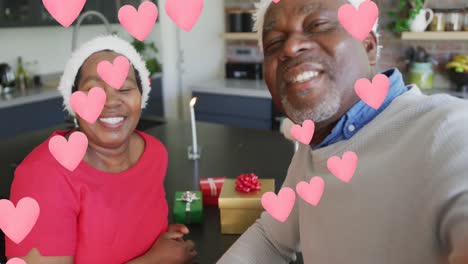 Animation-of-pink-hearts-over-senior-african-american-couple-in-santa-hats-at-christmas