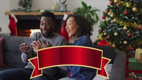 Animation-of-christmas-greetings-text-over-biracial-couple-using-smartphone-at-christmas