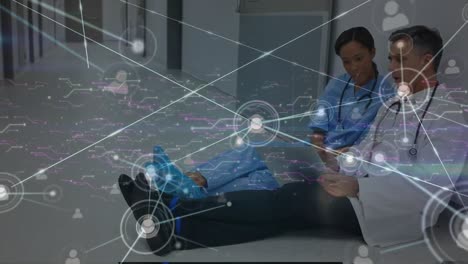 Animation-of-connected-dots-over-diverse-doctors-discussing-over-tablet-while-sitting-in-corridor