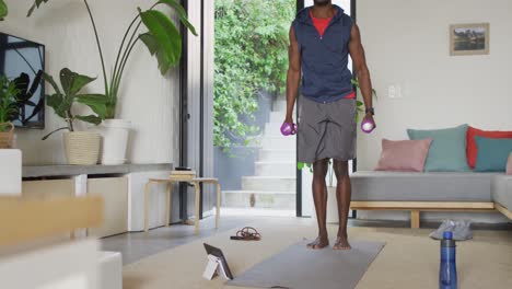 Happy-african-american-man-exercising-in-living-room,-using-tablet