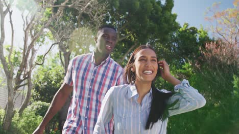 Video-of-happy-diverse-couple-holding-hands-and-walking-in-sunny-garden-smiling