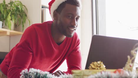 Happy-african-american-man-wearing-santa-hat,-using-laptop-for-video-call
