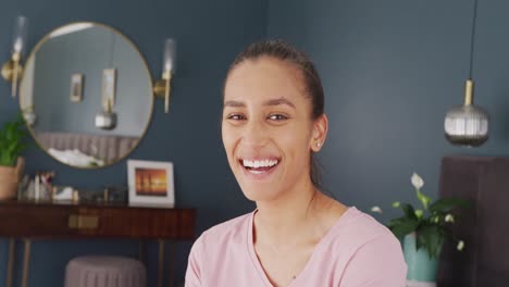 Video-portrait-of-happy-biracial-woman-smiling-to-camera-in-bedroom-at-home