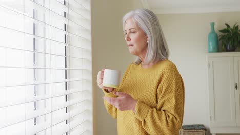 Senior-caucasian-woman-drinking-coffee-and-looking-through-window