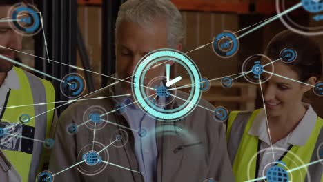 Animation-of-clock-connected-with-icons-over-caucasian-coworkers-discussing-in-warehouse