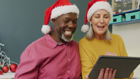 Happy-senior-diverse-couple-using-tablet-with-santa-hats