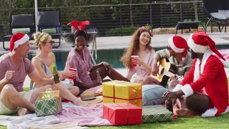 Feliz-Grupo-De-Amigos-Diversos-Tocando-La-Guitarra-En-La-Fiesta-De-Navidad-En-El-Jardín