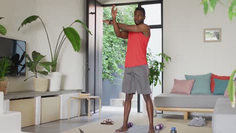 Happy-african-american-man-exercising-in-living-room,-stretching