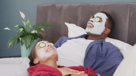 Video-Eines-Glücklichen,-Vielfältigen-Paares,-Das-Reinigende-Gesichtsmasken-Und-Gurken-Auf-Den-Augen-Trägt-Und-Lächelnd-Auf-Dem-Bett-Liegt