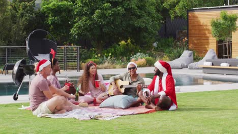 Happy-group-of-diverse-friends-playing-guitar-at-christmas-party-in-garden