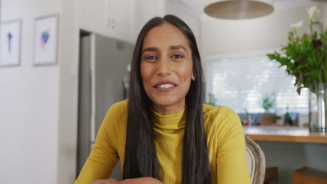 Video-of-happy-biracial-woman-making-video-call-gesturing-and-talking-to-camera-in-kitchen