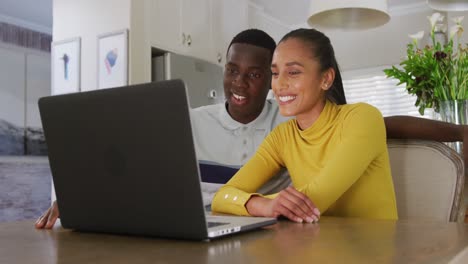 Video-Eines-Glücklichen,-Vielfältigen-Paares,-Das-Gemeinsam-Laptop-Schaut-Und-Lächelt,-Während-Es-In-Der-Küche-Sitzt