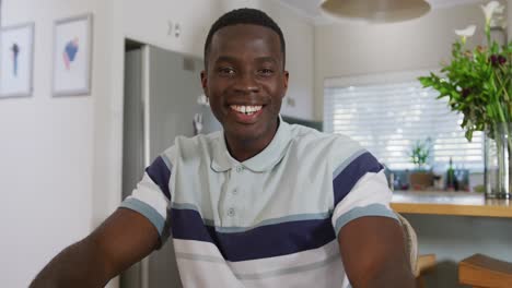 Video-Eines-Glücklichen-Afroamerikanischen-Mannes,-Der-Lächelnd-Einen-Videoanruf-Macht-Und-In-Der-Küche-In-Die-Kamera-Winkt