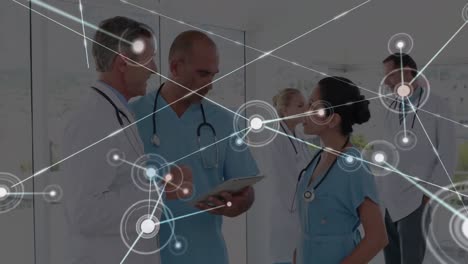 Animation-of-dots-connected-with-lines-over-multiracial-doctors-discussing-over-digital-tablet