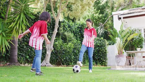 Video-of-happy-asian-mother-and-daughter-playing-soccer-in-garden