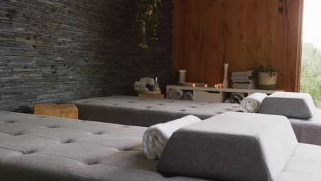 Vertical-video-of-massage-treatment-room-at-health-spa,-with-massage-tables-towels-and-lit-candles