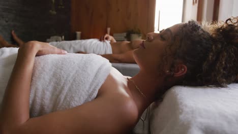 Video-of-relaxed-diverse-couple-in-towels-lying-with-eyes-closed-on-massage-tables-at-health-spa